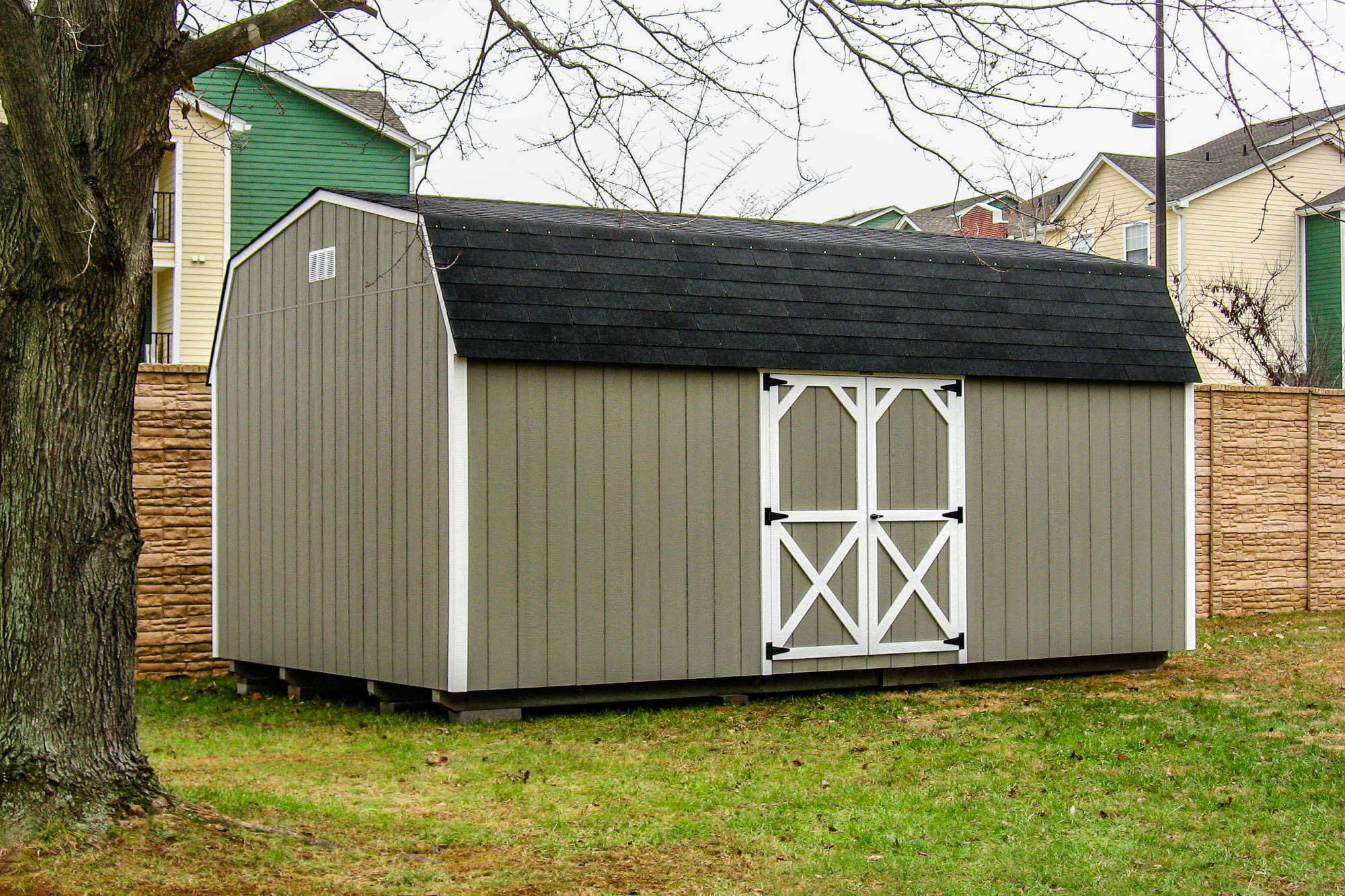 Gray barn-style shed with white trim and black shingles, placed in a residential backyard