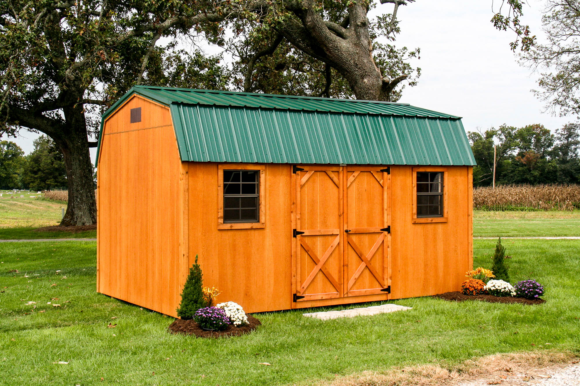 12x35 Wooden deluxe barn-style shed with green metal roofing and double barn doors, set on a landscaped lawn.