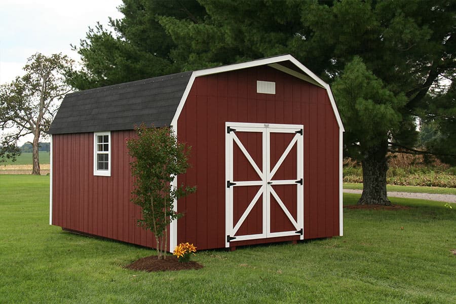 One of our 14x32 storage sheds - Red Barn Outdoor Shed with white trimmed double doors and white corners with matching side window beneath black gambrel style roof - shed sits on neat green lawn near trees