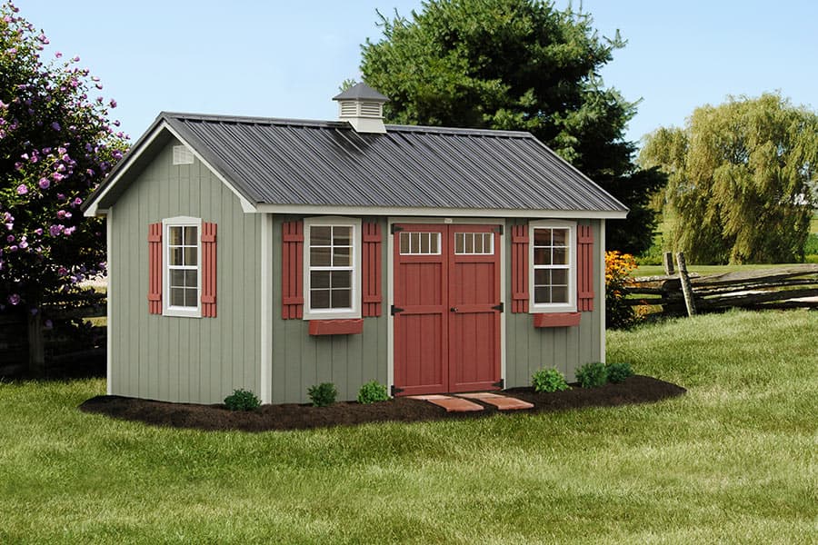 One of our popular storage sheds - Gray 14x32 Lancaster Shed with reddish brown double doors between two windows with matching colored shutters - As third matching window on the short wall of shed - Dark gray roof - shed sits on green grass near three visible trees