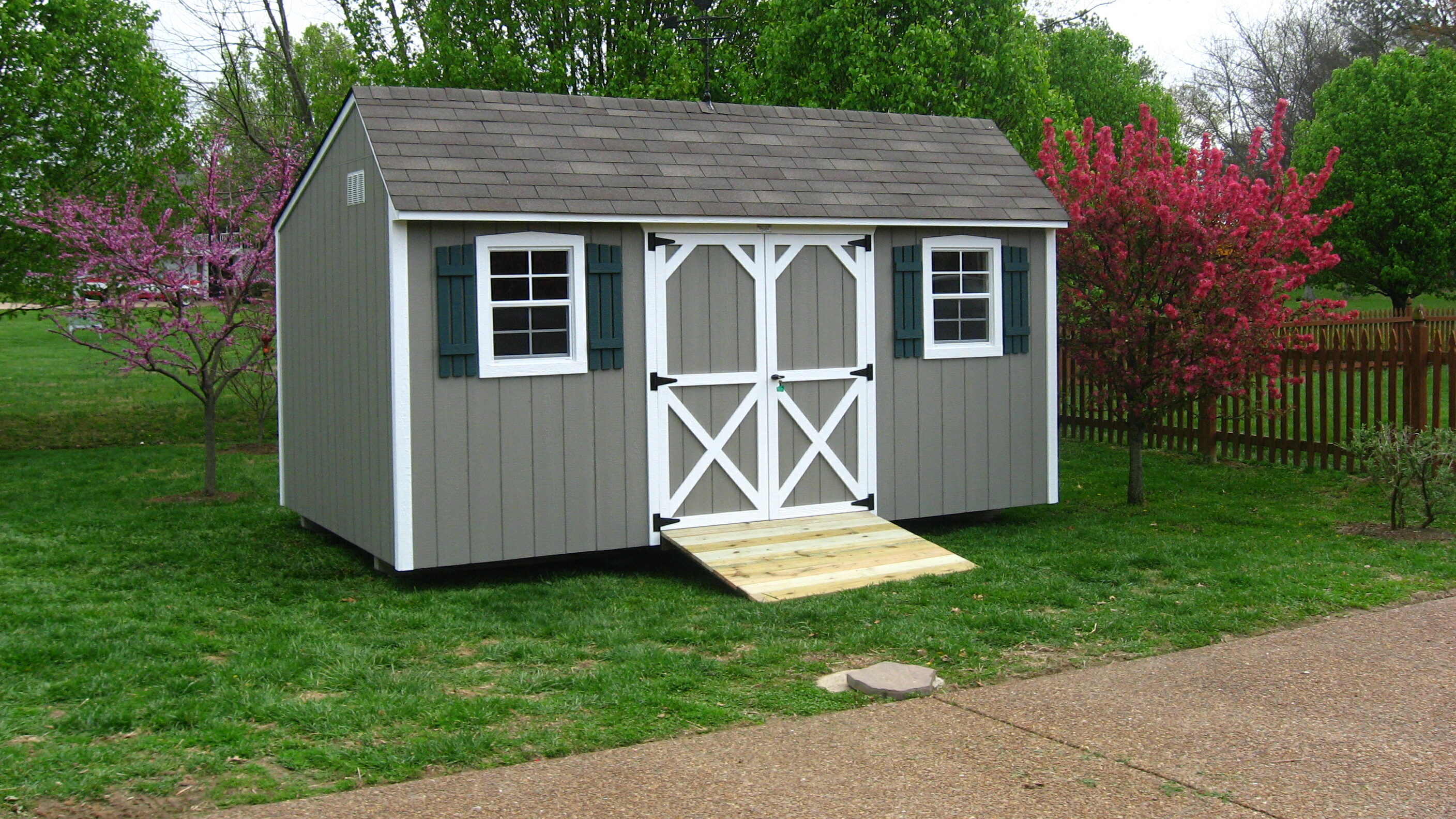 One of our 14x32 storage sheds - Gray Quaker Shed with white trimmed double doors between two windows with dark shutters under gray shingled rooof